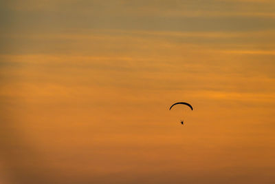 Low angle view of person paragliding against orange sky