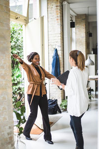 Happy female architect greeting coworker while entering in house