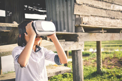 Girl wearing virtual reality simulator at field by log cabin