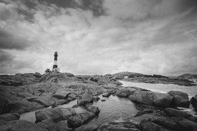 Lighthouse on rocky shore against cloudy sky