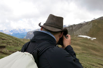 Rear view of male hiker photographing mountains against cloudy sky