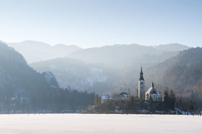 Scenic view of building by mountains against sky during winter