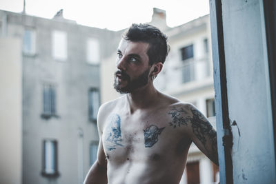 Portrait of shirtless man standing against wall