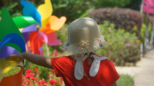 Rear view of girl in hat standing by multi colored pinwheel toy