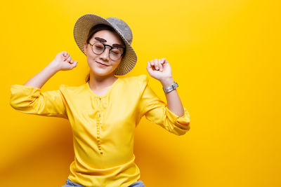 Woman wearing novelty glasses and hat against yellow background