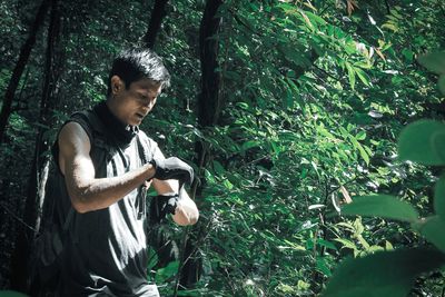 Young man standing by tree in forest