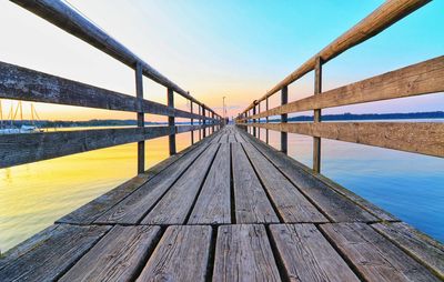 Wooden pier over river against sky during sunset