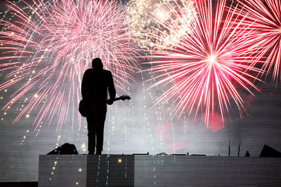 Silhouette of man playing guitar against firework display