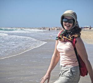 Portrait of happy young woman in sunglasses enjoying at beach against clear sky