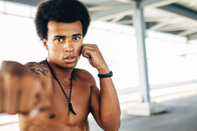 Portrait of shirtless young man punching below bridge