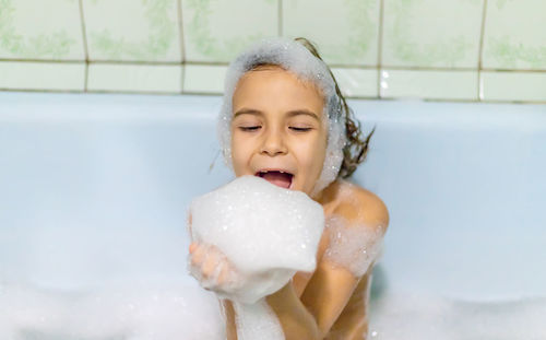 Playful girl playing with soap sud while taking bath in bathroom