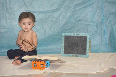 Portrait of shirtless boy sitting on bed