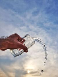 Low angle view of cropped hand holding drinking glass against sky during sunset