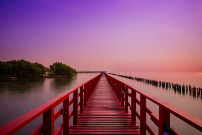 Wooden bridge over lake against sky during sunset