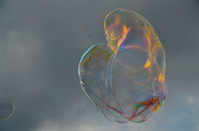 Low angle view of bubbles in mid-air against cloudy sky