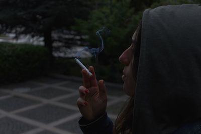 Close-up of woman in hooded shirt smoking cigarette