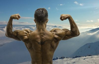 Rear view of shirtless man standing snowcapped mountain