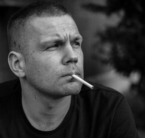 Close-up of man with cigarette looking away while sitting outdoors