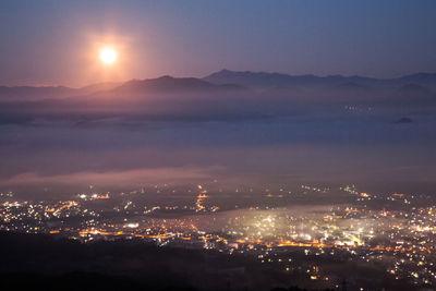 Illuminated city and mountains against sky during sunset