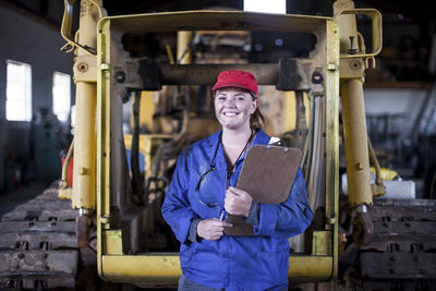 Portrait of smiling woman holding clipboard in workshop