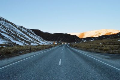 Empty road leading towards mountains against clear sky