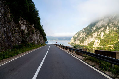 Empty road leading towards mountains against sky