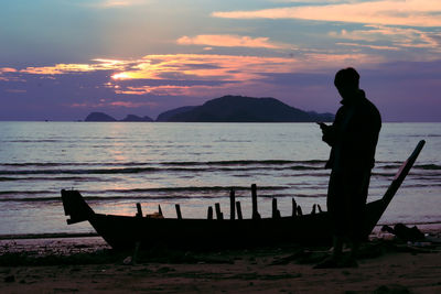 Silhouette man standing by boat at beach during sunset