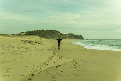 Rear view of man standing on beach against sky