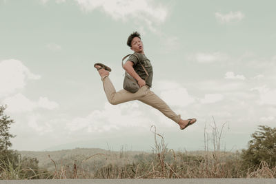 Young man jumping on field against sky