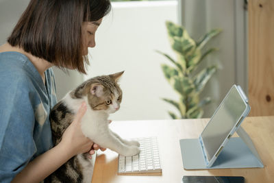 Asian woman play with her cat and use tablet meeting and working from home