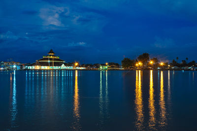 Illuminated buildings by sea against sky at night