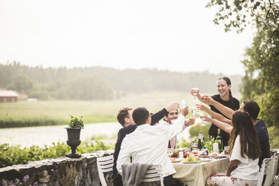 Cheerful male and female friends toasting wineglasses during dinner party in backyard