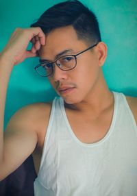 Close-up portrait of young man with eyeglasses standing against wall
