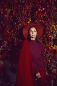 Woman in a red hat and red sweater stands on a background of orange leaves grapes wall autumn