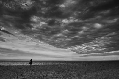 Silhouette people at beach against cloudy sky