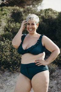 Positive curvy female with short hair in swimwear walking looking at camera on sandy path on beach and enjoying summer