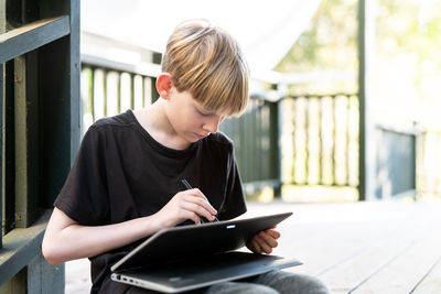 Tween sitting outside on porch using touch screen tablet with stylus