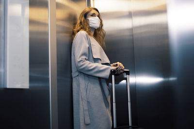 Low angle view of young woman carrying suitcase in elevator