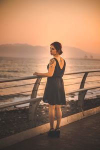 Portrait of woman standing at promenade against clear orange sky