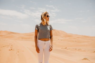 Woman standing on sand dune in desert against sky