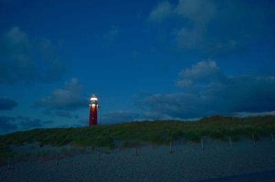 Illuminated lighthouse at beach against sky