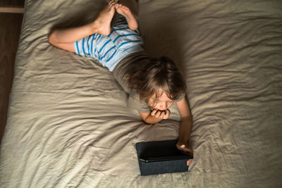 Boy lying on the bed using digital tablet computer playing games or watching cartoons at home.