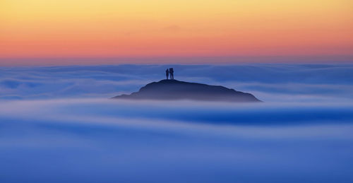 People standing on mountain peak amidst cloudscape during sunset