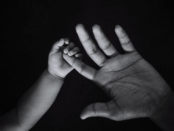 Close-up of baby holding mother hand on black background