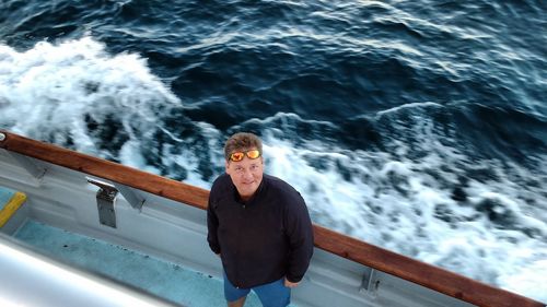 High angle portrait of man standing at sailboat