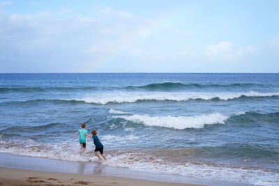 Young boys playing in the waves with a rainbow over the ocean on ka'anapali beach in hawaii. 