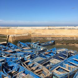 Boats moored at harbor against blue sky