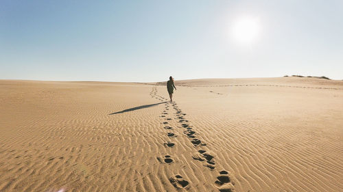 Person walking on sand dune in desert against clear sky