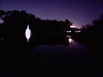 Silhouette trees by lake against sky at night