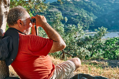 Rear view of tourist man looking through binoculars at the mountains view. hiking, unity with nature